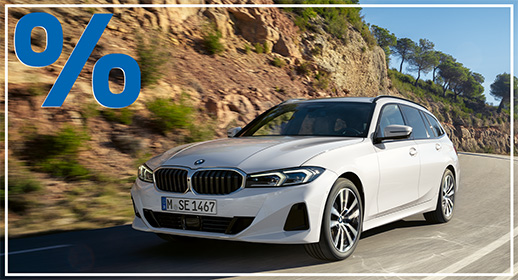 Hellgraue BMW 318i Limousine parkend auf einem Asphaltplatz vor Gebirgssilhouette in der Dämmerung; blaues Prozent-Symbol oben links.