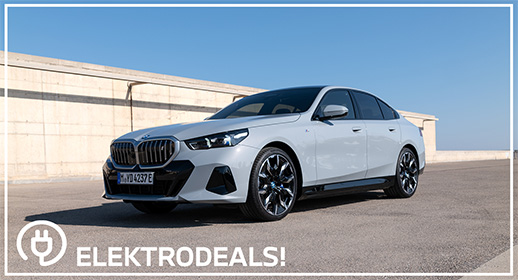"Dreiviertel-Vorderansicht einer hellgrauen BMW i5 Elektro-Limousine mit Kennzeichen 'MDY 237E', parkend auf Asphalt vor einer Betonmauer. Mit 'Elektrodeals!'-Logo."