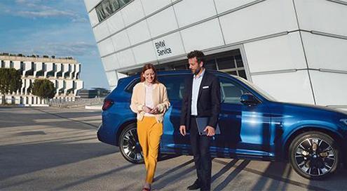 Frau und Mann gehen lächelnd vor einem BMW Service Gebäude mit einem blauen BMW SUV.