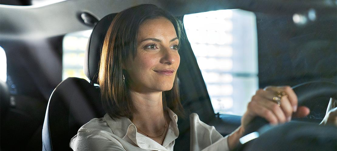 Probefahrt BMW Rhein  Eine lächelnde Frau fährt ein Auto und blickt zur Seite.
