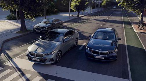 Drei BMW Limousinen stehen auf einer Straße in einer städtischen Umgebung.