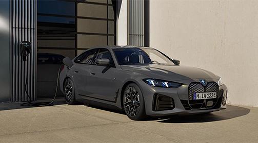 Ein grauer BMW i4 Gran Coupé wird an einer Ladesäule vor einem modernen Gebäude aufgeladen