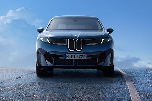 Eine Frontansicht eines dunkelblauen, sportlich wirkenden Fahrzeugs (BMW iX3) der "Neuen Klasse" auf einer Straße, mit einem blauen Himmel im Hintergrund.