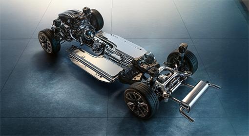 BMW Plug-in-Hybride Das Bild zeigt das Fahrgestell eines Autos von schräg oben. Die Karosserie fehlt, sodass die mechanischen und elektrischen Bauteile sichtbar sind. In der Mitte ist die flache Batterie des Plug-in-Hybrids zu erkennen, während an der Vorder- und Rückseite die Aufhängungen, Räder, Bremsen und der Auspuff sichtbar sind.