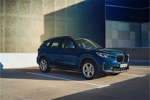Ein dunkelblauer BMW X1 steht alleine auf einem Parkplatz. Das Licht wirft starke Schatten einer hohen Wand auf den Boden, was eine kontrastreiche, moderne Atmosphäre schafft. Der Fokus liegt hier auf dem Design der Verbrenner-Variante.