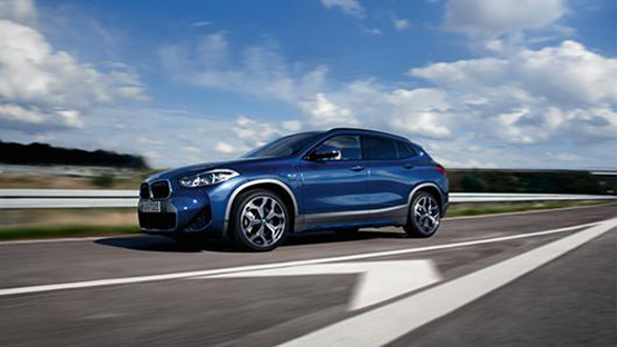 BMW Elektroauto gebraucht Blauer BMW X2 SUV fährt auf einer Straße mit blauem Himmel.